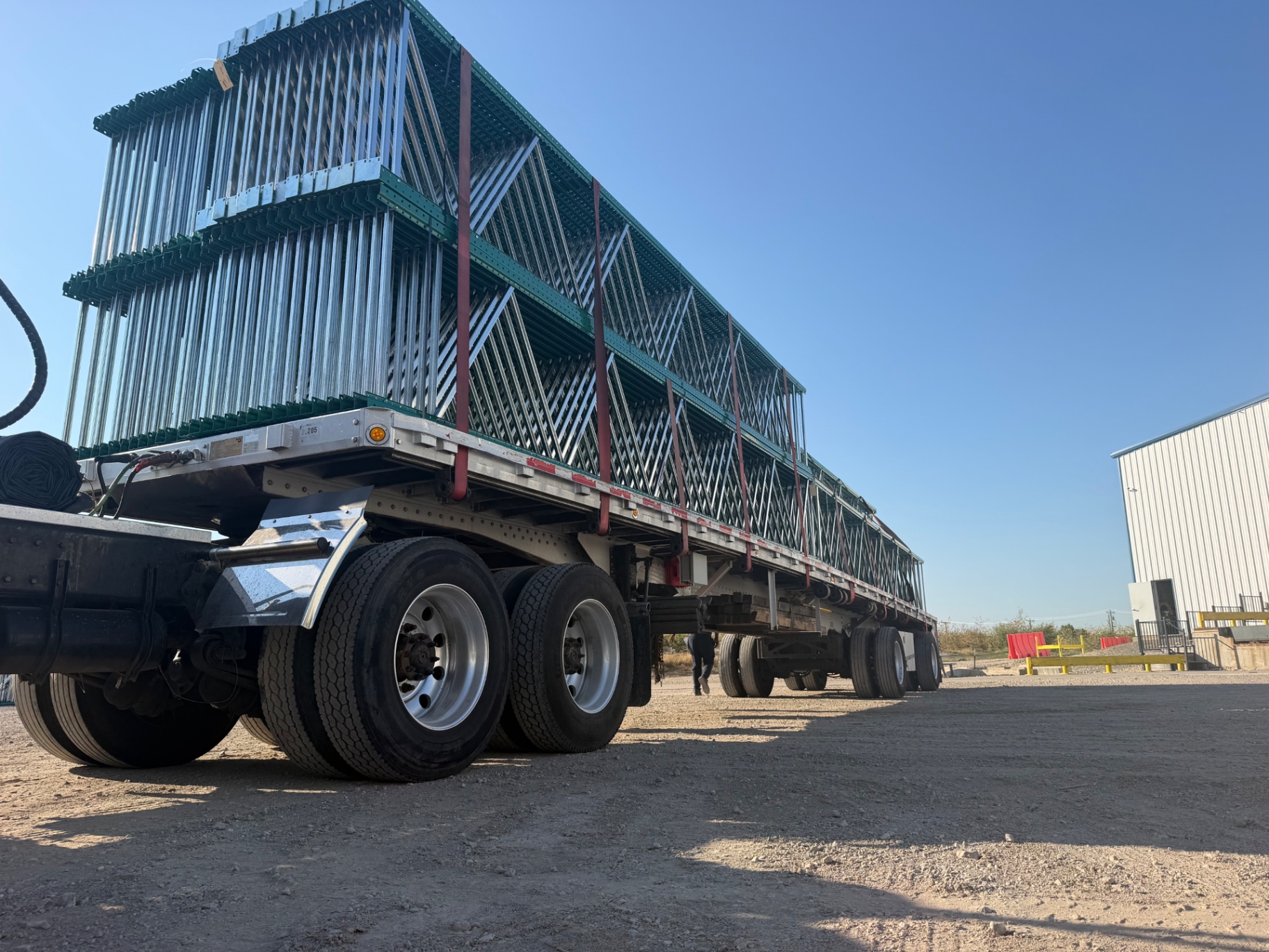 Flatbed trailer loaded high with green cantilever rack uprights at the NAWL yard