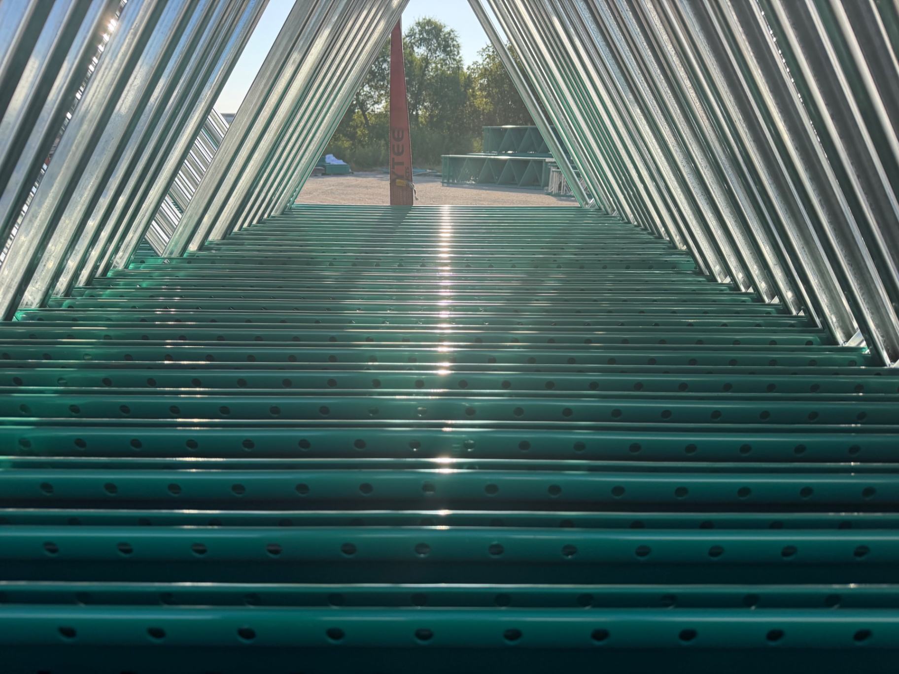 Rows of green cantilever rack arms catching sunlight, shot through the steel